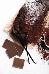 Chocolate cake with cocoa powder, vanilla pods on white table