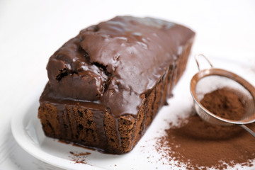 Chocolate cake with icing and cocoa powder on white table