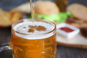 Glass mug of draft light beer with snacks on dark wooden table, close up