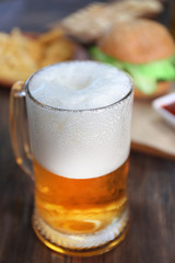 Glass mug of light beer with snacks on dark wooden table, close up