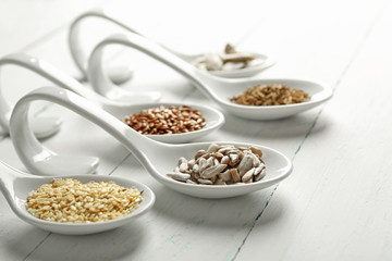 Different kinds of seeds in spoons on wooden table