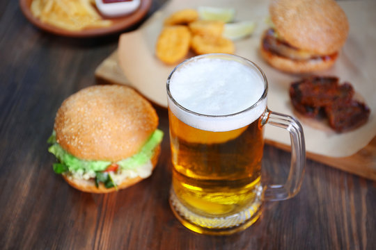 Glass mug of light beer with hamburgers on dark wooden table, close up