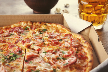Tasty pizza in carton and glass of beer are on wooden table, close up
