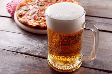 Tasty pizza and glass of beer are on wooden table, close up