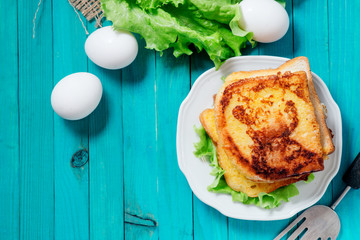 
sandwich with cheese and mayonnaise fried in egg with lettuce on a wooden background