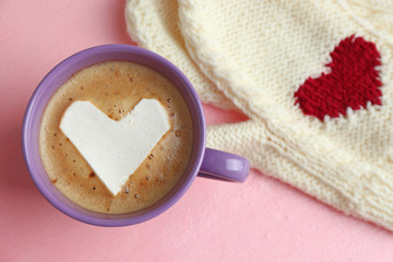 Cup of hot cappuccino with heart marshmallow and warm mittens on pink background, close up