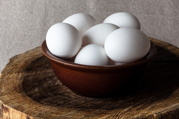 White eggs in a brown clay cracked bowl on wooden old weathered cracked cutting board on rough beige rural map from side