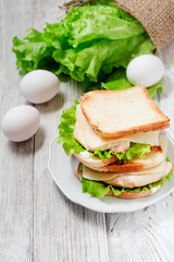 
sandwich with chicken breast , egg, lettuce, cheese and mayonnaise on a wooden background