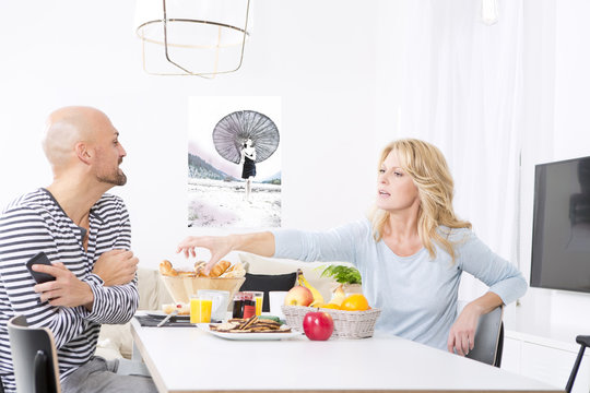 Couple at breakfast table, woman displeased with husband using smartphone