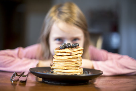 Plate with stack of pancakes with little girl in the background