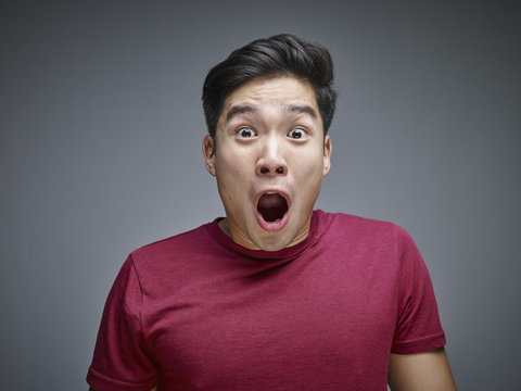 Portrait of shocked young man in front of grey background