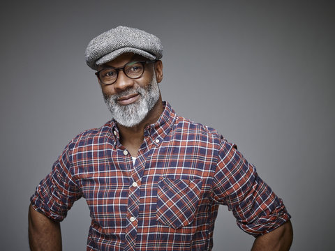 Portrait of smiling man wearing cap and spectacles in front of grey background