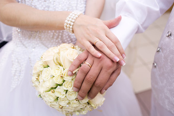 Hands with wedding rings and bridal bouquet
