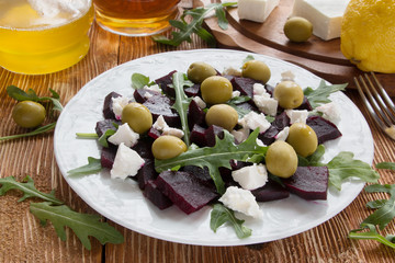 Beet (beetroot) salad with cheese, olives and arugula on the white plate. Olive oil and lemon dressing. On the wooden table.