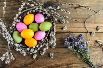 Easter background, selective focus. Homemade hand painted colorful easter eggs in nest from willow branches close-up over retro wooden rustic background