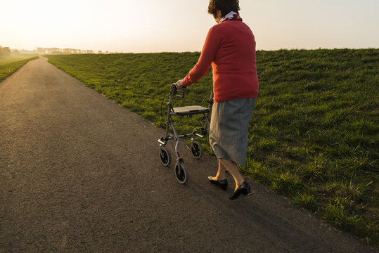 Senior woman walking with wheeled walker on a path