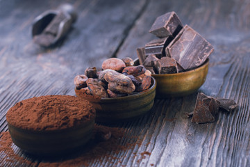 Dark chocolate pieces, cocoa powder and cocoa beans on a wooden table