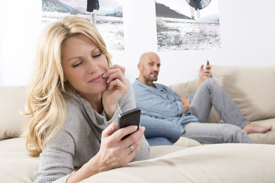 Mature couple sitting on sofa using their smart phones