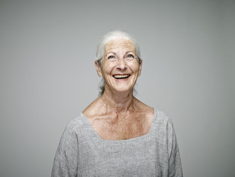 Portrait of laughing senior woman looking up in front of grey background