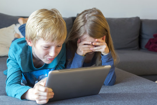 Boy and girl lying on the couch using digital tablet