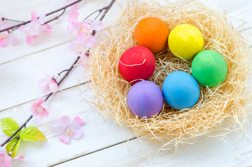 Fototapeta na wymiar Colorful easter eggs at brown nest on white wooden table