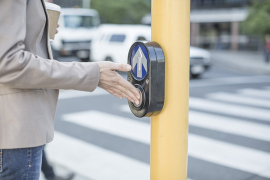 Woman waiting to cross a city street, pressing pedestrian crossing button