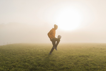Young man playing soccer on meadow in the evening