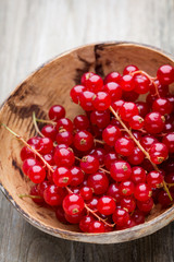 Redcurrant on a branch close to a wooden bowl.