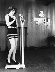 Profile of a young woman measuring her weight on a weighing scale 