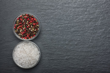 White salt and pepper in a glass bowl on black stone background