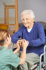 Seniorin im Rollstuhl hält Hände mit Krankenpflegerin