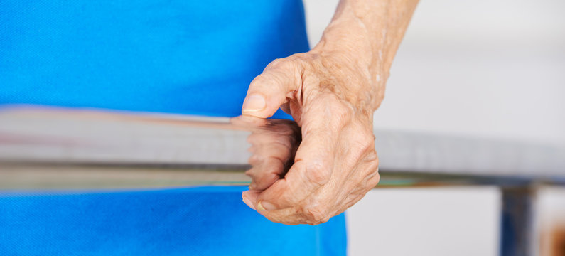 Faltige Hand einer Seniorin am Geländer