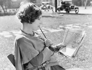 Woman with a pencil in her mouth reading the newspaper 