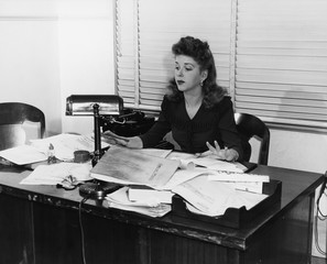 Kobieta pracuje przy biurkiem zakrywającym w papierach - 104428803