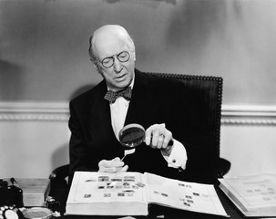 Senior man examining a postage stamp with a magnifying glass 