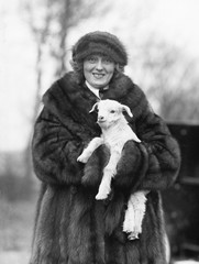 Woman in a fur coat and hat holding a small baby lamb in her arms 