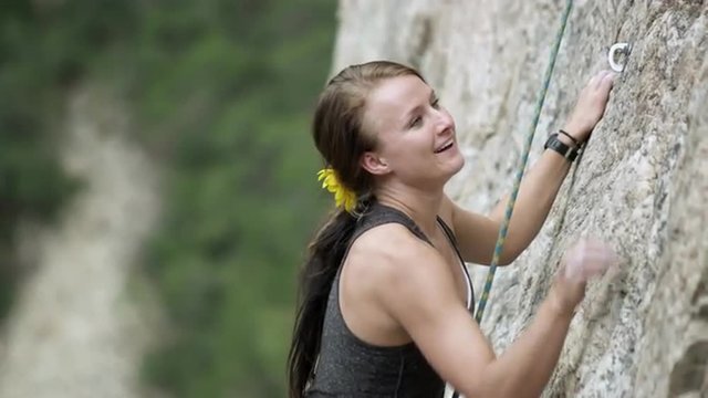 Rock climbing woman, with dreads, nearing her friends at the top.