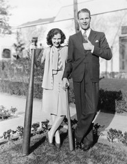 Couple standing together with one oversized baseball bat 