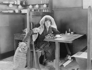 Young woman sitting in a booth in a diner, trying to steal something out of a jute bag 