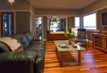 Contemporary upscale home living room interior with leather couch, glass coffee table, window seat and windows with water views