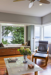 Contemporary upscale home living room interior with leather lounge chair, glass coffee table, window seat and windows with water views