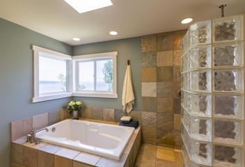 Contemporary upscale home spa bathroom interior with glass tile shower, slate tile walls, acrylic soaking tub, skylight and view windows