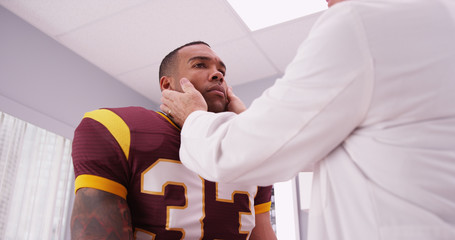 Mid aged doctor checking football player's sports neck injury