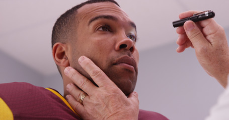 Mid aged doctor checking football player's eyes with flashlight © Mark Adams