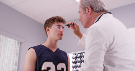 Senior medical doctor checking basketball player's eyes with fla