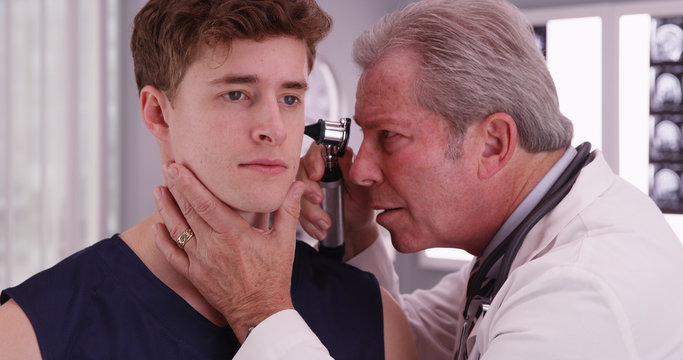 Senior doctor checking sports athlete's ear with an otoscope