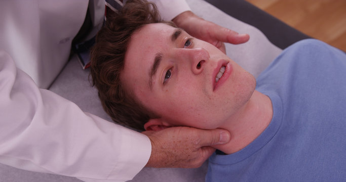 Young adult male with chiropractor examining neck pain