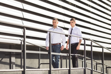 Two young businessmen are coming to work. They are approching to a modern office building using the ramp.