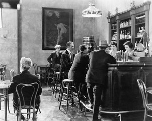 Men sitting around a counter in a bar  - obrazy, fototapety, plakaty