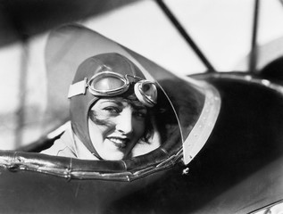 Young woman sitting in a biplane with hat and gargles  - obrazy, fototapety, plakaty